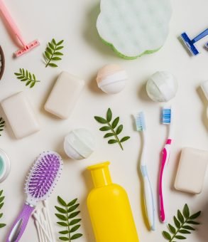 cosmetic-products-with-salt-toothbrush-razor-hairbrush-leaves-white-backdrop